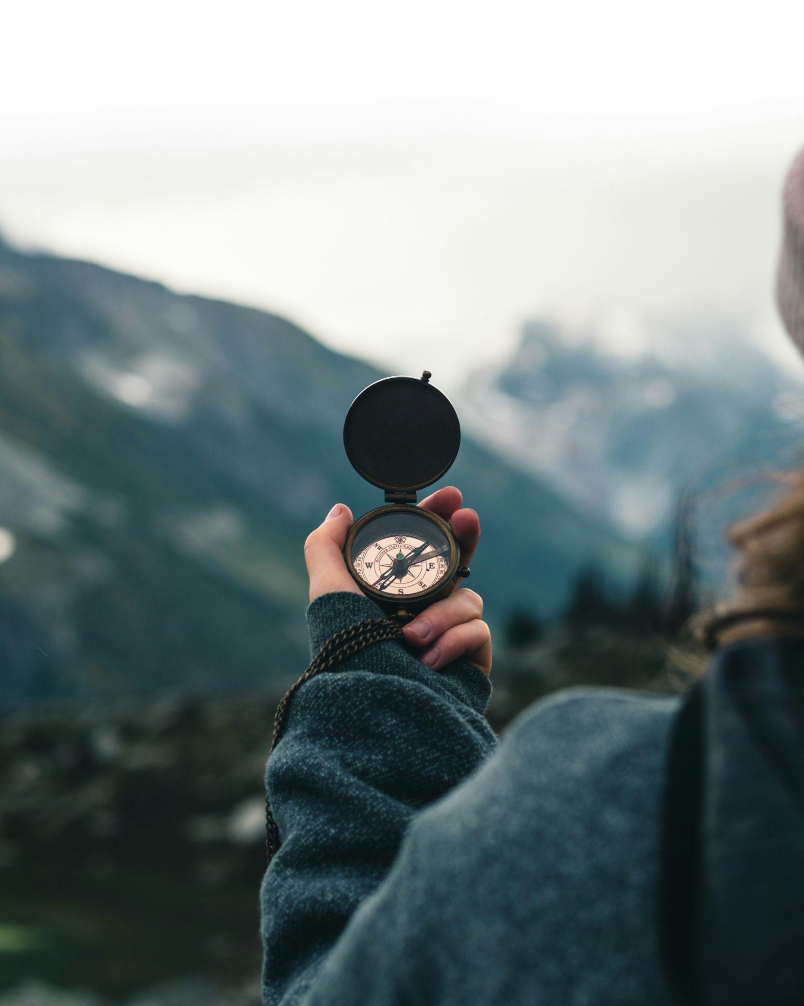 Hand mit Kompass vor einer Bergkulisse